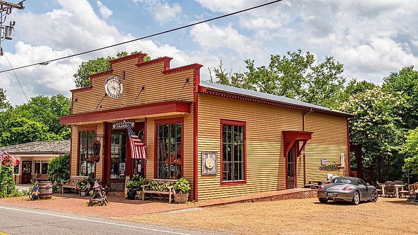 Historic red-trimmed storefront in Leipers Fork, Tennessee, with American flags, wooden benches, and a classic car parked outside on a sunny day.