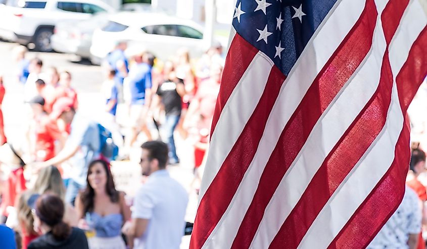 People gathering on Main Street for the annual 4th of July parade with a US flag in foreground in Barrington, Illinois.