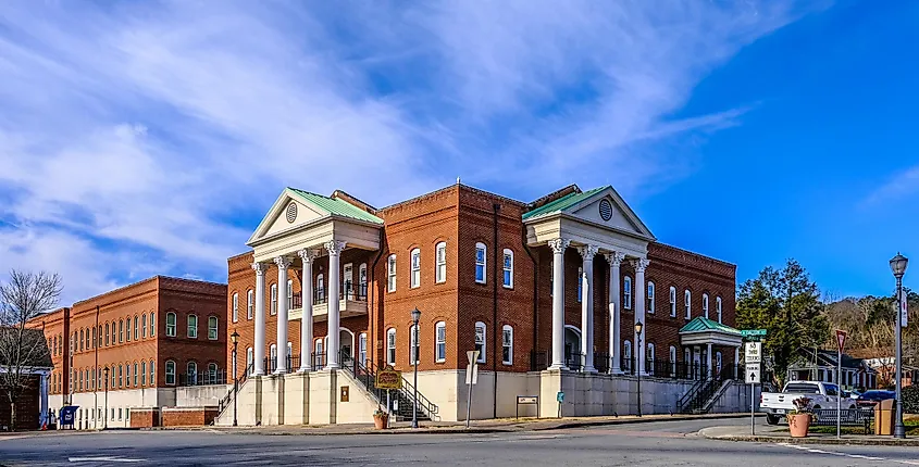 A majestic red-brick building with white columns stands under a blue sky. The structure exudes a classical, stately presence on a sunny day.