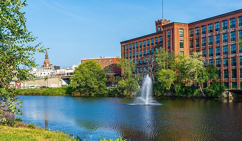 Fountain on the Nashua River against the background of a historic cotton factory building with a clock tower in the old industrial park of Nashua