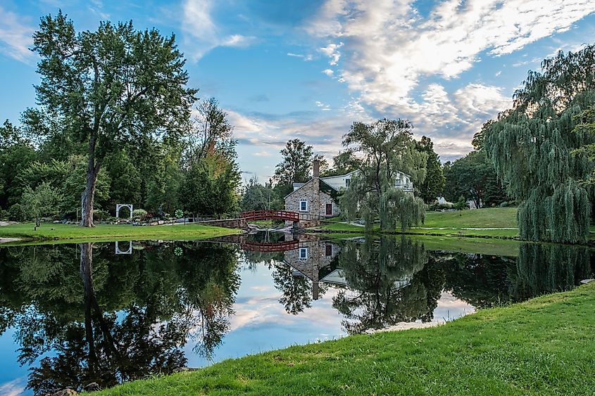 A picturesque view over the pond with a perfect reflection in the water of the trees, grass, red footbridge and old stone house. Editorial credit: John Fader / Shutterstock.com