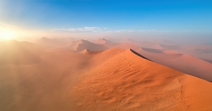 Aerial view of the vast orange dunes of the Namib Desert lit by sunrise. 