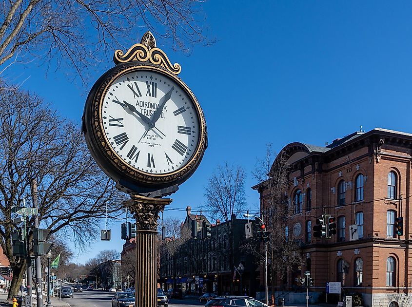 Landscape view of Adirondack Trust Company's double-faced street clock on Broadway in Saratoga Springs, NY, USA, with City Hall visible across the street.