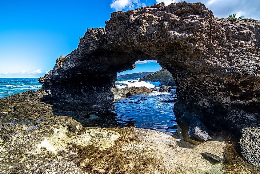 Rocky shoreline at Kea'au Beach Park in Oahu, Hawaii, with waves crashing against the lava rocks and ocean views in the background