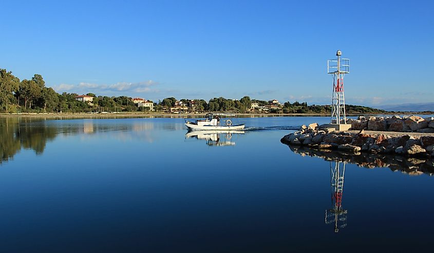 Small white wooden fishing boat entering the port of Koronisia village in Ambracian gulf in Greece near the beacon at summer