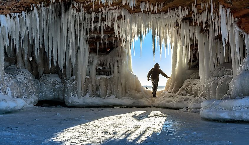 A person steps through an icicle-laden hole in the sandstone formations on Wisconsin's Apostle Islands National Lakeshore near Meyer's beach; Lake Superior.