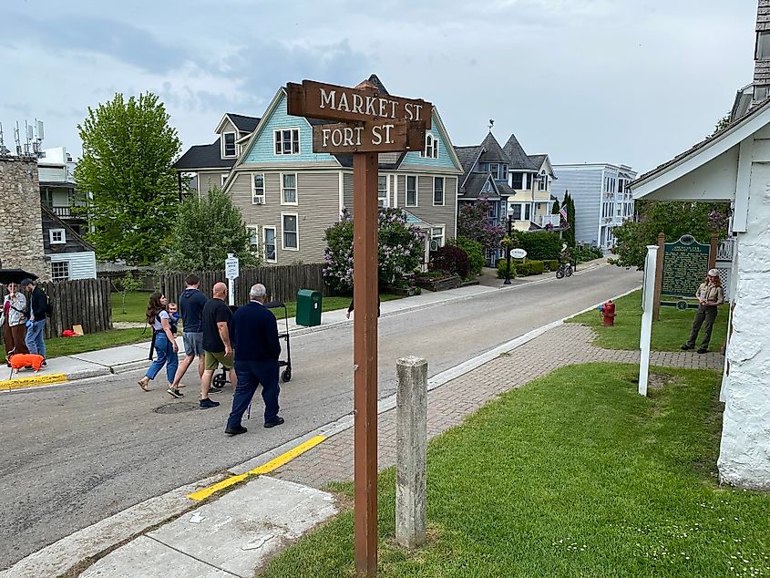 A multigenerational family walk freely on a quite street with a park ranger and museum interpretive signs seen on the right hand side.