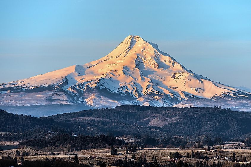 Sunrise view of Mount Hood, Oregon forest, and a village nestled in the picturesque landscape.