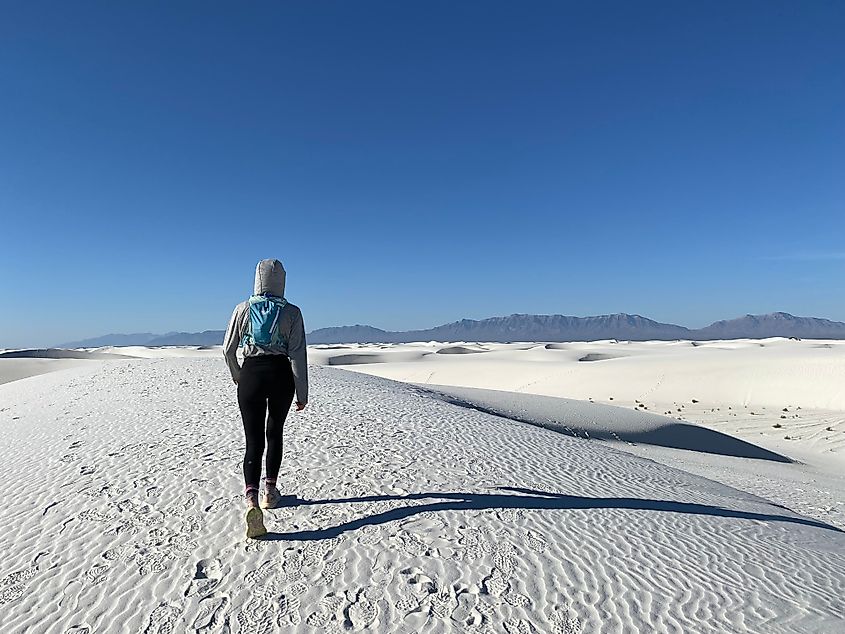 A hiker covered with a hoody crosses the gypsum dune fields at White Sands National Park, inching closer to the distant mountains.