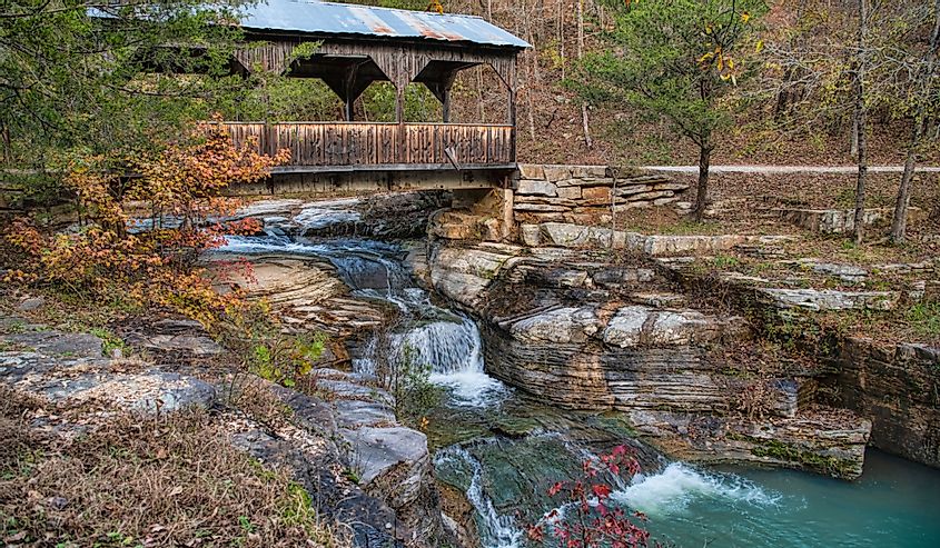 Quaint-covered bridge over a cascading waterfall in autumn in Ponca, Arkansas.