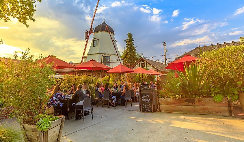 People at a coffee shop enjoy picturesque Danish architecture of Solvang. Old Windmill at sunset. Santa Ynez Valley in Santa Barbara County.