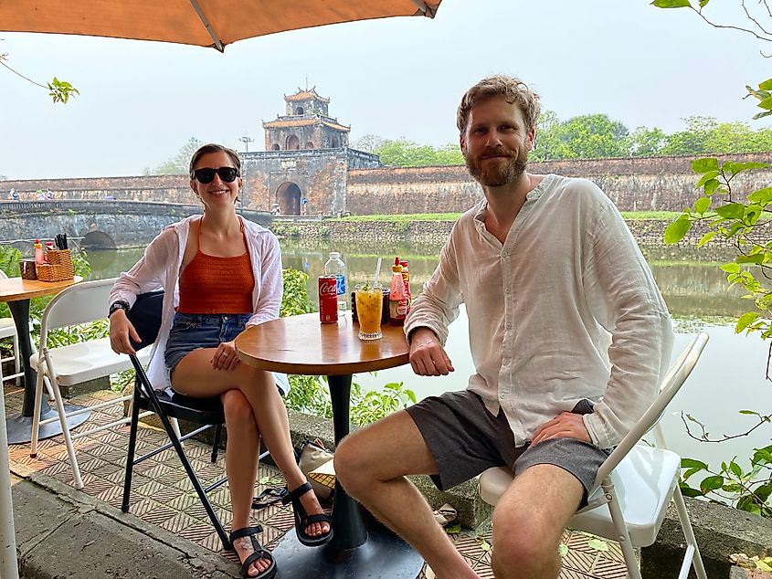 A young male and female sitting at a riverside cafe with an ancient walled city in the background.