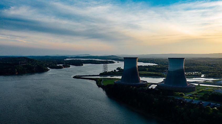 Cooling towers near river under cloudy sky at sundown