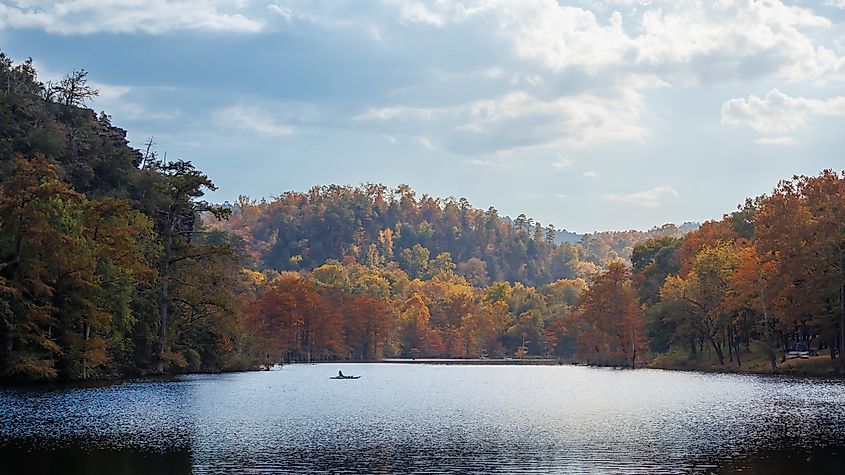 Serene Autumn Lake in Broken Bow, Oklahoma, with a Lone Boat and Vibrant Trees. Credit: Zion_Zhu/Shutterstock.com