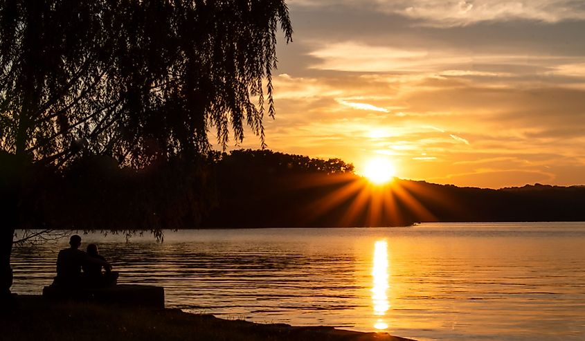 Couple sitting under a tree silhouetted by the setting sun on Watts Bar lake in East Tennessee at Camp John Knox.