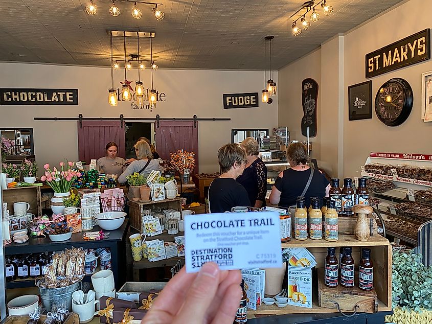 Holding up a Chocolate Trail ticket from within the decorative St. Marys Chocolate shop
