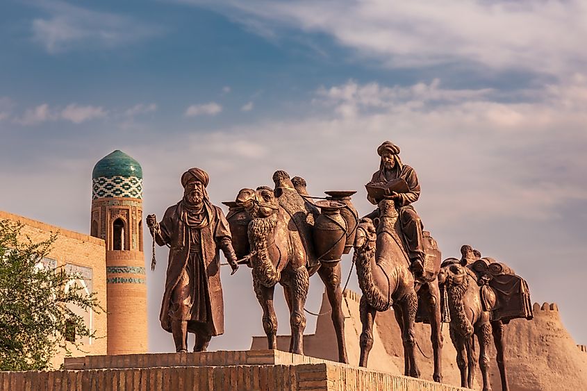 Sculpture group of an ancient caravan with camels carrying various goods along the Silk Road and two men in traditional Uzbek dress in front of the old city walls
