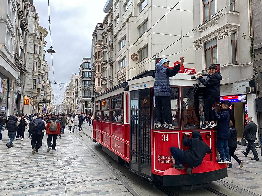 A crew of boys hitching a ride on the back of a red trolley as it works its way down a pedestrian shopping street in Istanbul.