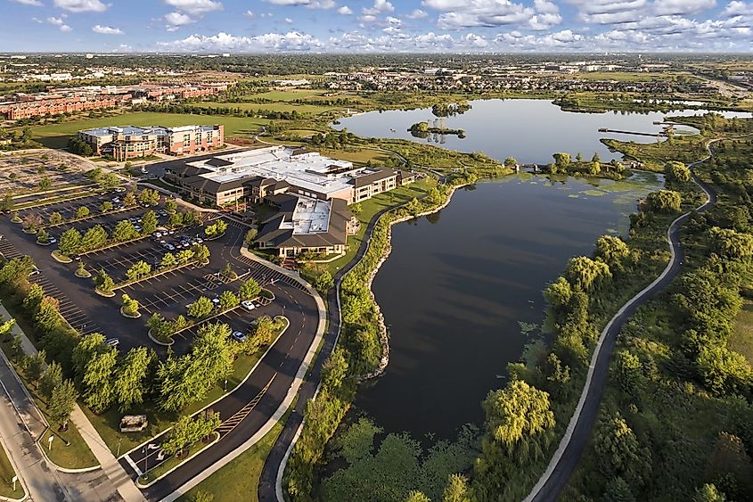Aerial view of a lake beside a community center and grade school with walking paths and bridge at The Glen in Glenview, Illinois.