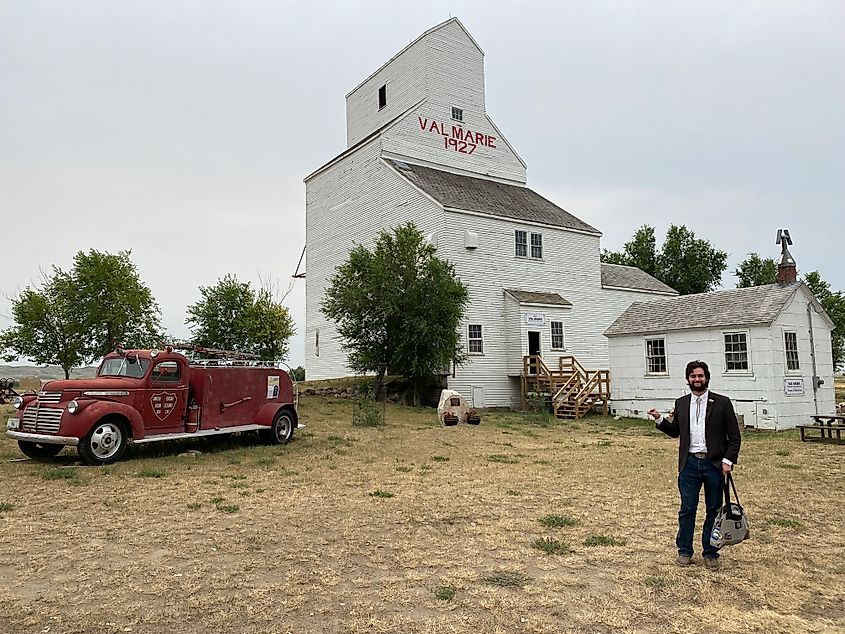 A male tour guide stands in front of an old grain elevator with the name and year inscribed: Val Marie 1927