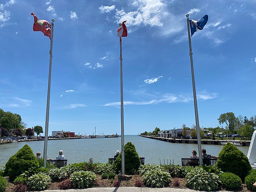 Three sets of couples occupying three benches beneath three flag poles at the head of a town's river