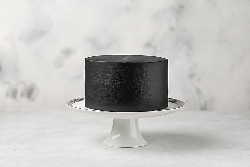 A plain black cake on a cake stand with a white background.