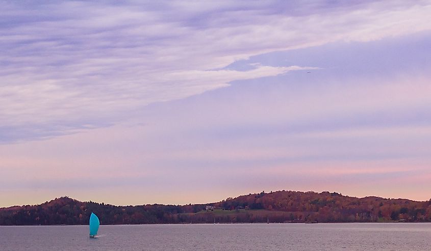 A sail boat on Shelburne Bay in Lake Champlain, Vermont during autumn colors and purple sky