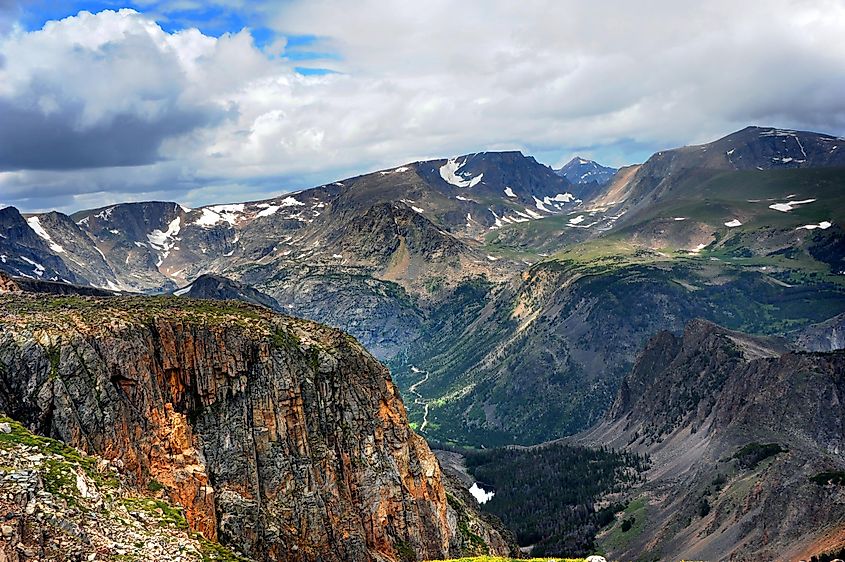 View from the top of Beartooth Pass in Wyoming, featuring Absaroka Mountain peaks, a valley, a distant river, and mostly cloudy skies.