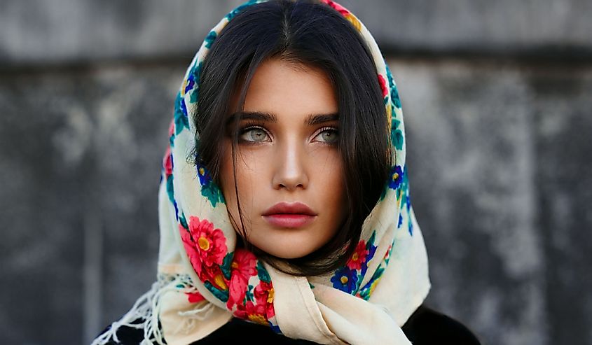 Portrait of fashionable young woman with perfect make up posing in colorful Russian shawl on her head