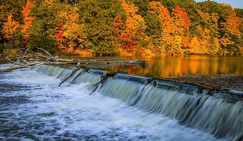 The Grand River surrounded by vibrant autumn foliage and small waterfall at the Fitzgerald County Park in Grand Ledge, Michigan.