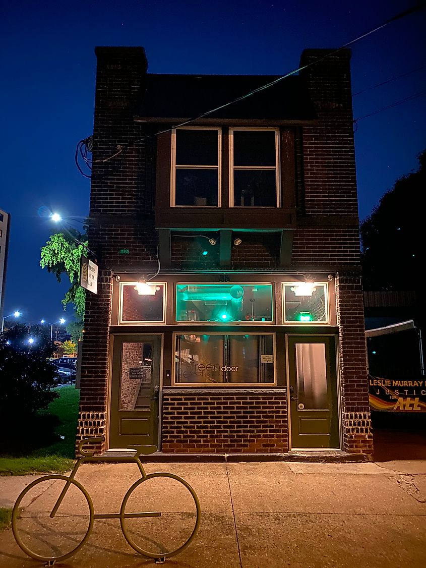A bicycle sculpture stands in front of a dark brick building, illumined in green, at night. 