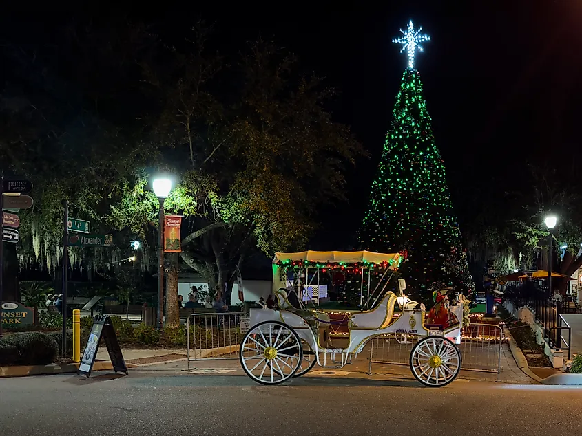 Mount Dora, Florida: A motorized white carriage parked in a town square with a driver in traditional dress, a tall Christmas tree with green lights, baubles, and a nutcracker doll