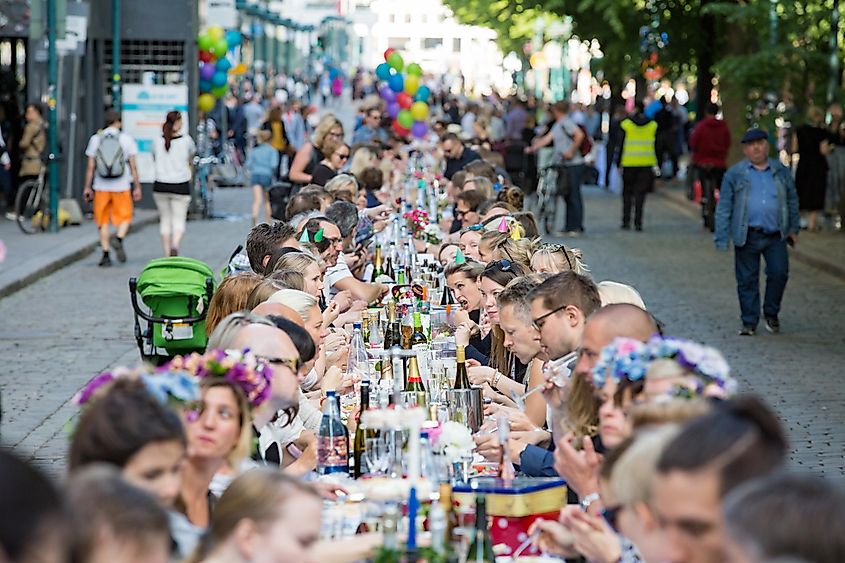 Long table with lots of people eating and drinking together. The Day of City Celebration in centre of Helsinki. Finnish your dinner under the sky.