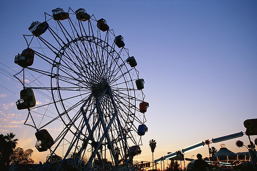A Ferris wheel lit up at a fairground at dusk.
