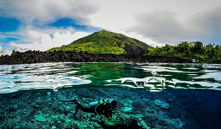 Diver below the surface in Banda, Indonesia underwater photo with mountain in the background