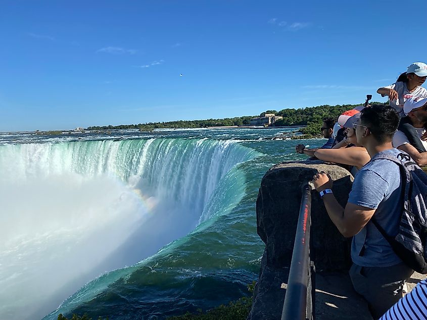 A group of Asian tourists gather beside a railing above Niagara's powerful and misty waterfall known as Horseshoe Falls.
