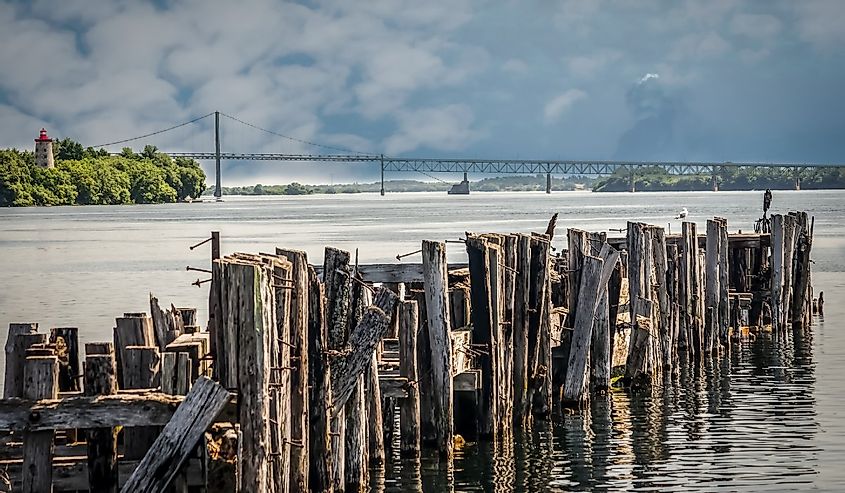 Antique Pilings from an old port with an 1800's lighthouse and International bridge across the St. Lawrence River on a cloudy day