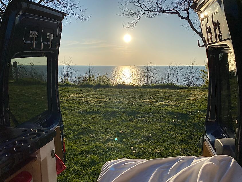 The view out the back of a camper van parked atop a lakeside hill, watching the late afternoon sun start to set.