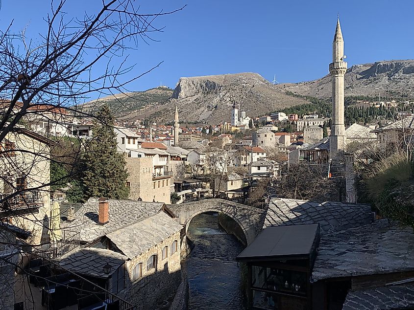 Mountains backdrop the Old Town of Mostar. The smaller of the two bridges shares the frame with mosque spires and other antiquitous structures.