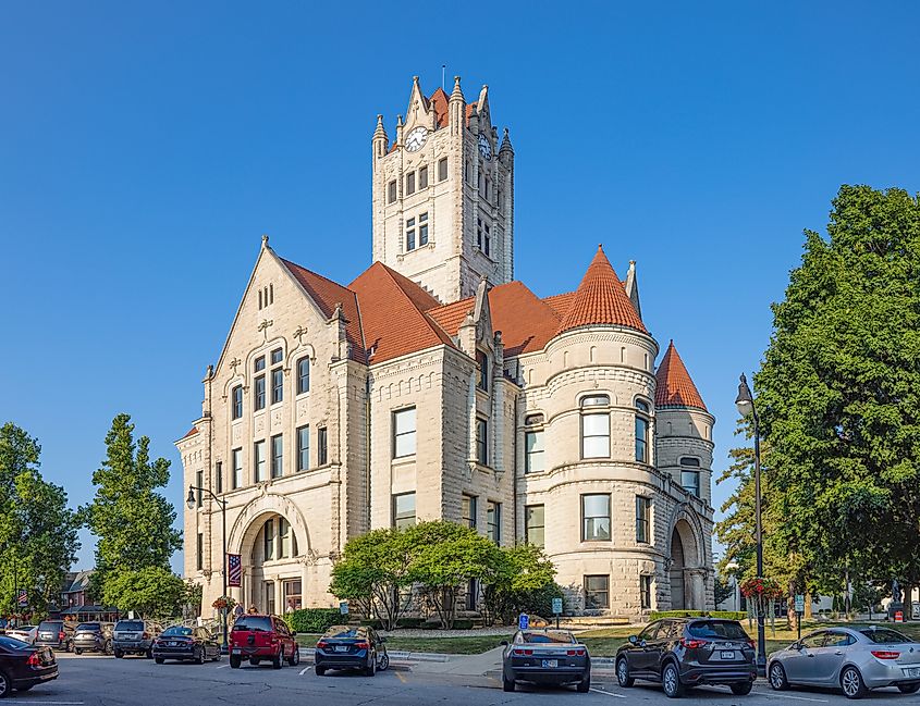 Historic courthouse with red-tiled roofs, ornate towers, and arched windows under a clear blue sky; cars parked in front.