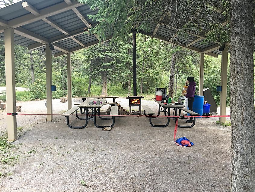 A woman making dinner by a campsite fire beneath an overhang.