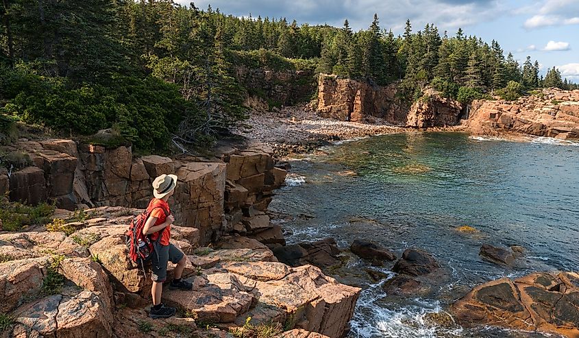 Hiker standing on a rock overlooking the water, taking in the views in Acadia National Park