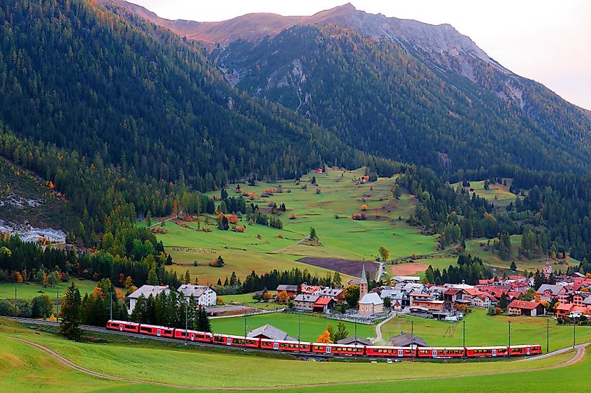 A Rhaetian train (RhB) traveling through the grassy meadow and Bergün Village (AaronChenPS2 via Shutterstock)