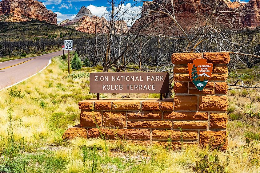 Stone monument entrance sign marking Kolob Terrace Road against red rock peaks in Zion National Park. Editorial credit: Photo Spirit / Shutterstock.com