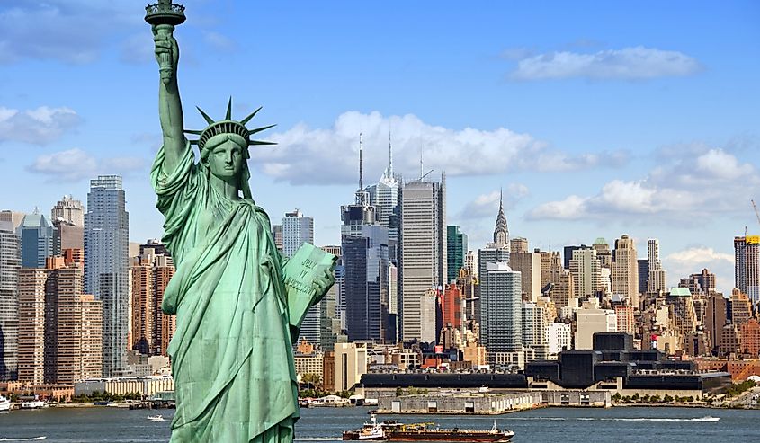 New York City skyline with Statue of Liberty over Hudson River. with midtown Manhattan skyscrapers and freight sailing ship in USA.