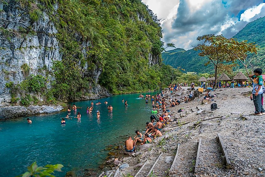 Tourists swimming and relaxing in turquoise natural river pool surrounded by rocky cliffs and tropical mountains in Pozuzo Peru.