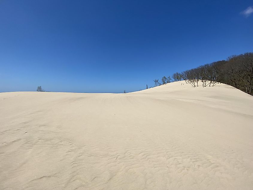 A pristine yet hulking sand dune leads toward a clear blue sky