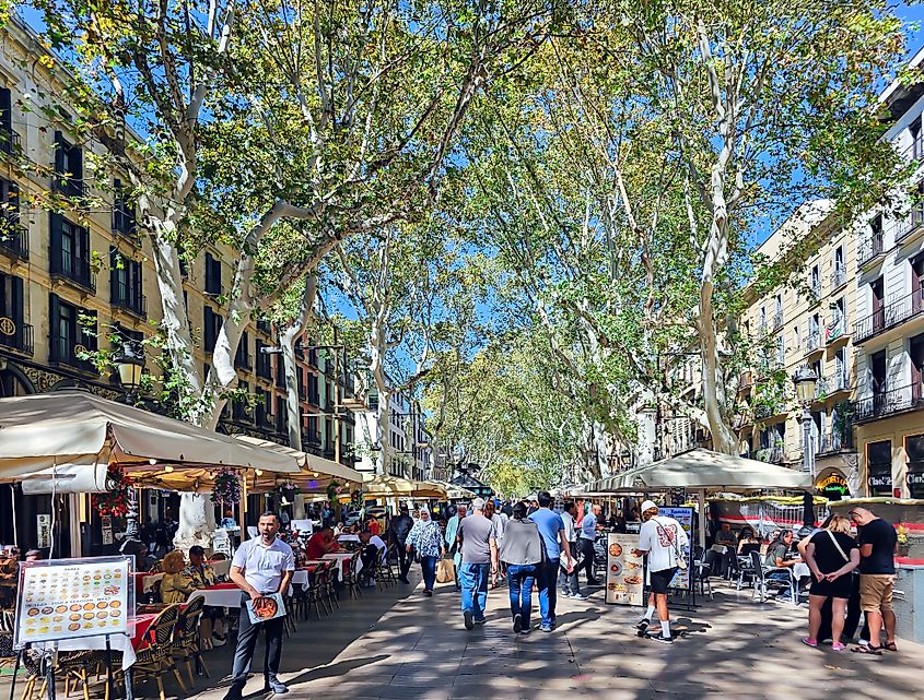 Pedestrian street La Rambla with tourists and various cafes under the shade of plane trees in Barcelona, Spain. Editorial credit: Tanya Keisha / Shutterstock.com