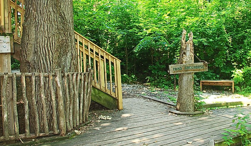 Sign post and steps to Tom’s tree house as seen from a boardwalk walking trail, through the lush woods in the Fontenelle Forest Nature Center in Bellevue, Nebraska near Omaha.