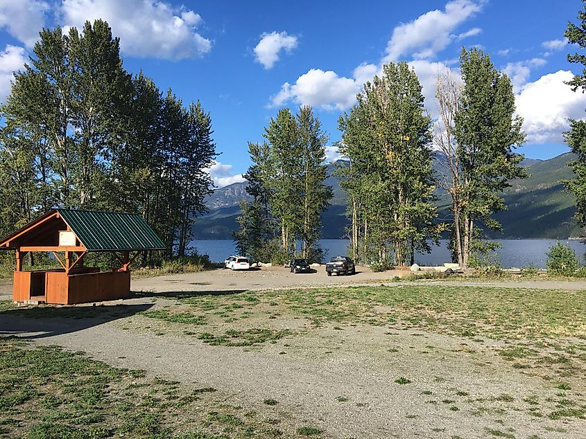 A dirt parking lot with a few vehicles, with the large, blue Kootenay Lake in the background.